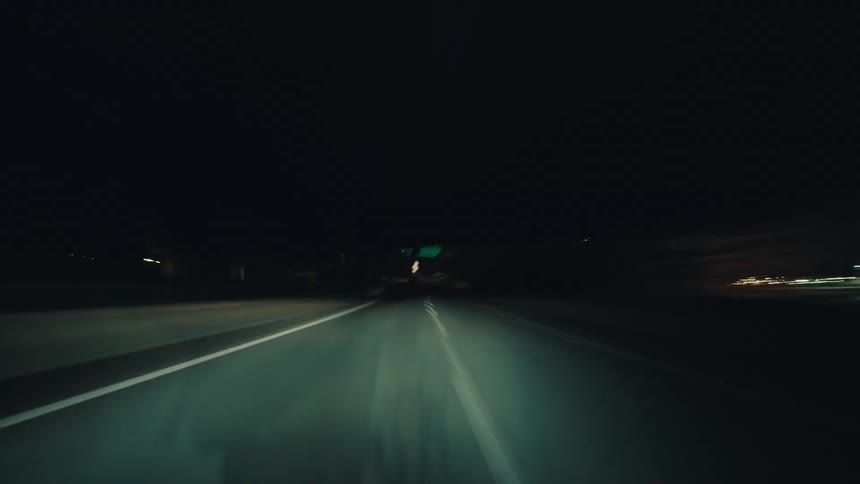 Fast-paced hyper-lapse shot from a car speeding down an empty highway at night with blurry light trails
