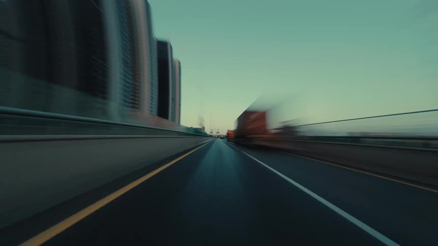 A moody, cinematic hyper-lapse captures a high-speed drive on a modern expressway through a city and past an industrial port at dusk