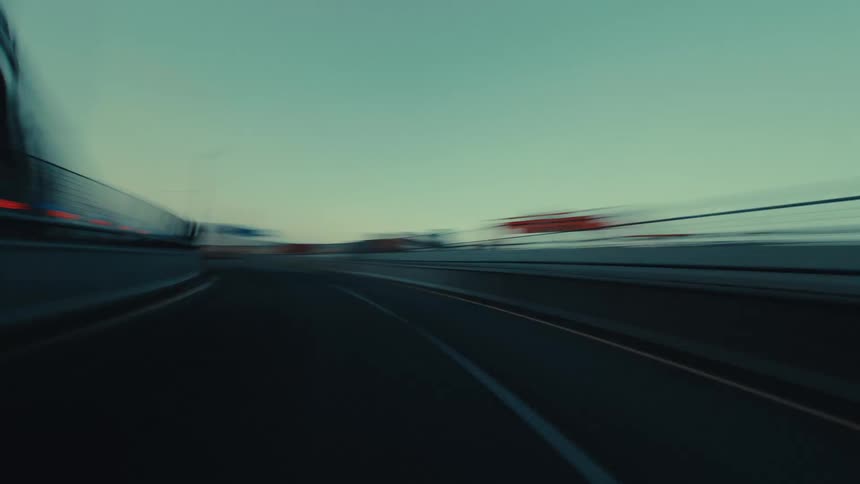 A moody, cinematic hyper-lapse captures a high-speed drive on a modern expressway through a city and past an industrial port at dusk