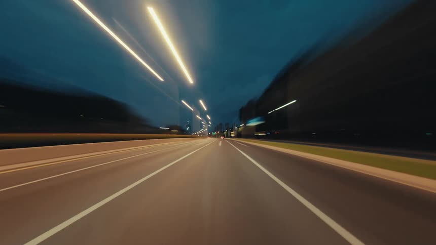 A dynamic point-of-view time-lapse of driving through a futuristic city highway at night, surrounded by streaking light trails