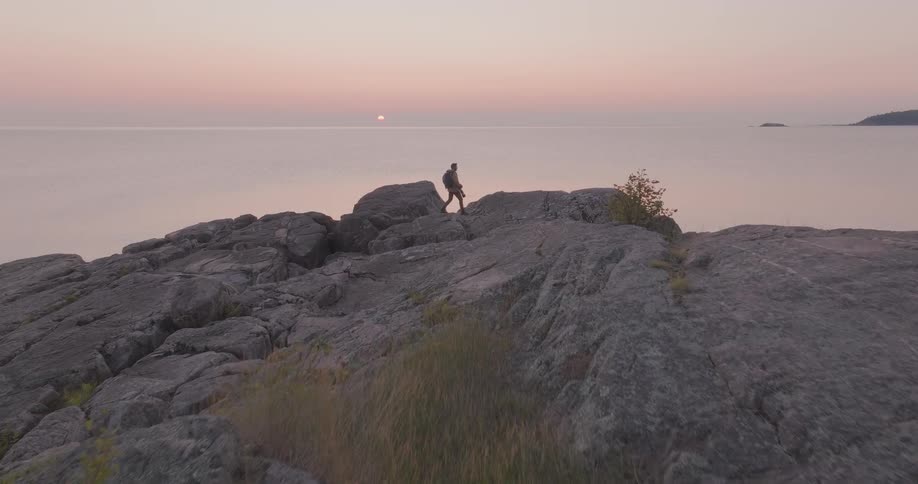 Aerial view of a male photographer hiking across a rocky shoreline to watch the sunrise over the tranquil water