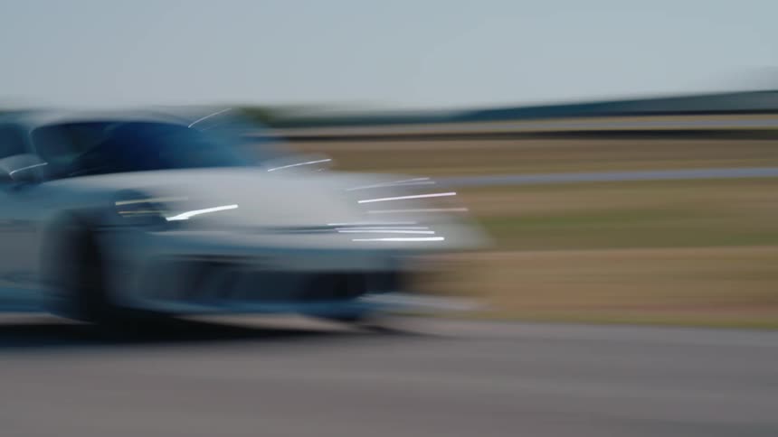A white sports car creates a motion blur effect as it speeds around a racetrack on a sunny day