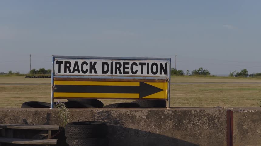 A 'Track Direction' sign with a large arrow sits beside an empty racetrack under a clear sky