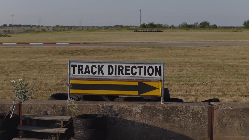 A 'Track Direction' sign with a yellow arrow points the way on an empty race course as the camera slowly pulls back