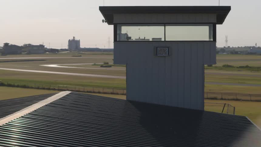 A slow aerial pullback revealing a small air traffic control tower overlooking a quiet airport runway on a clear day