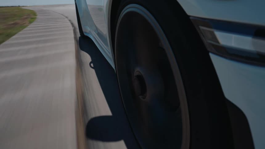 A close-up, low-angle view of a luxury white sports car's front wheel spinning rapidly on a sunny racetrack