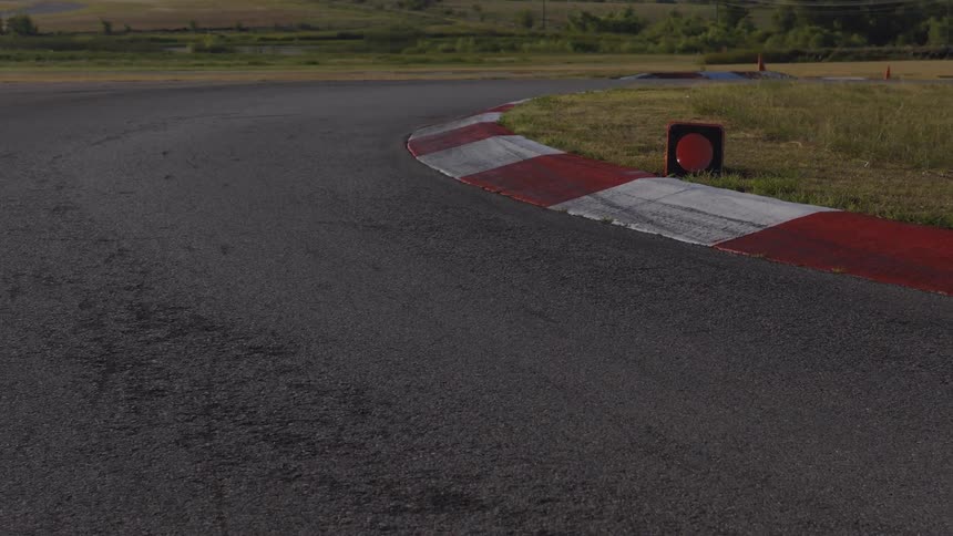 A slow dolly shot approaches a red and white curb on an empty asphalt racetrack