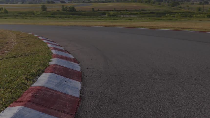 A slow dolly shot follows the painted red and white rumble strip around an empty racetrack corner