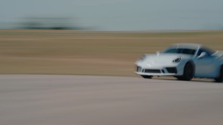 A sleek white sports car blurs past the camera at high speed on a professional racetrack