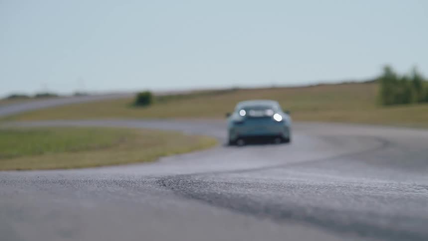 A silver sports car speeds away down a winding racetrack on a sunny day