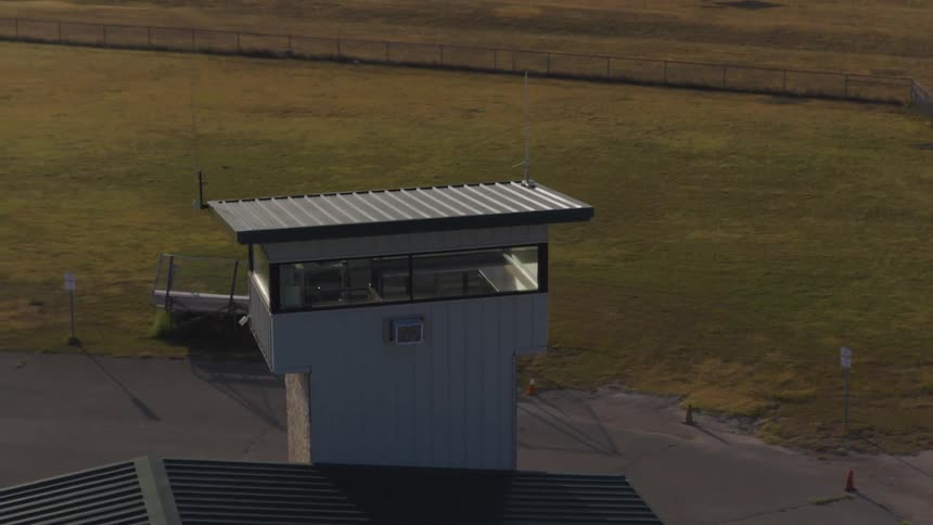 An aerial shot slowly zooms out from a small, empty observation tower at a rural airstrip during golden hour