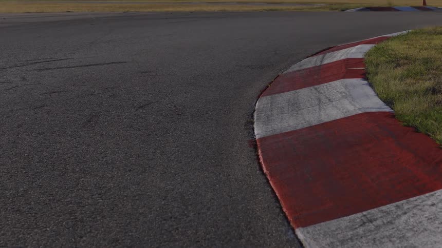 A slow-moving, low-angle shot along the red and white curb of a sharp turn on an empty racetrack