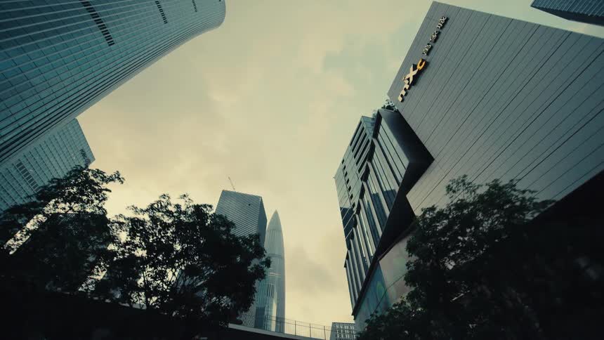 A smooth low-angle tracking shot glides backward through a modern city, passing under a bridge surrounded by towering skyscrapers