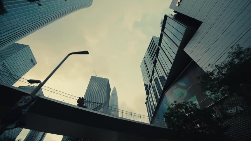 A smooth low-angle tracking shot glides backward through a modern city, passing under a bridge surrounded by towering skyscrapers