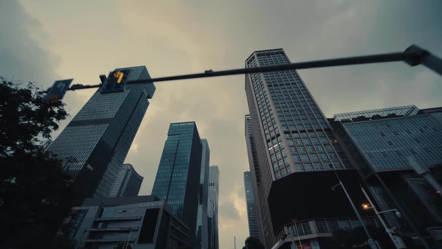Driving through a modern downtown metropolis while looking up at imposing skyscrapers under a gloomy, overcast sky