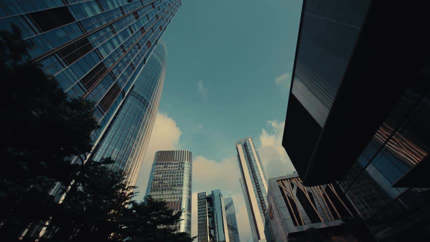 A cinematic low-angle dolly shot reveals towering modern glass skyscrapers against a bright blue sky