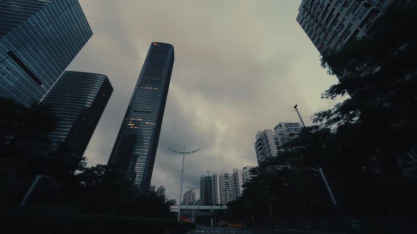 A moody low-angle point-of-view shot driving through the streets of a modern city with towering skyscrapers