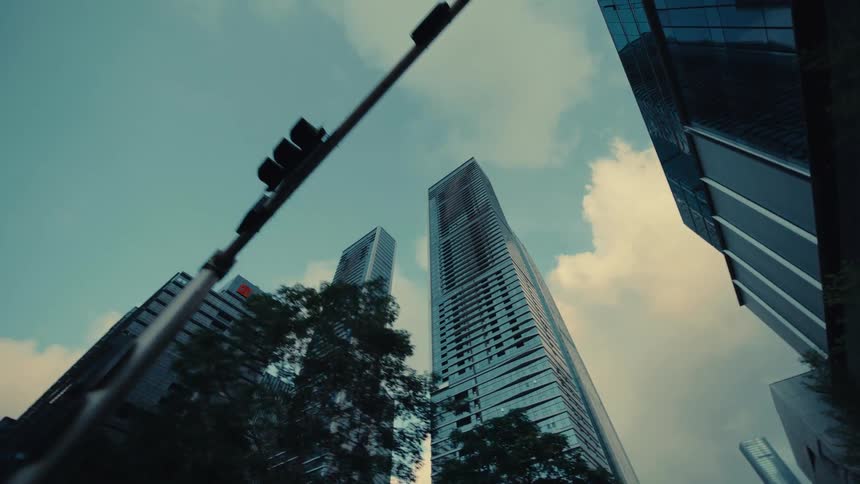 A slow, low-angle tracking shot reveals the towering glass facades of modern skyscrapers in an urban financial district