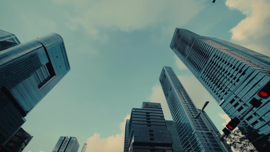 A slow, low-angle tracking shot reveals the towering glass facades of modern skyscrapers in an urban financial district