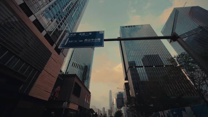 A slow dolly shot through a modern city center, looking up at the towering glass skyscrapers against a warm, golden sky