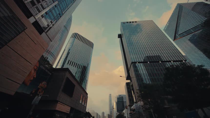 A slow dolly shot through a modern city center, looking up at the towering glass skyscrapers against a warm, golden sky