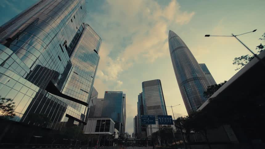 A low-angle dolly shot slowly moves through a modern city financial district, looking up at impressive glass skyscrapers against the sky
