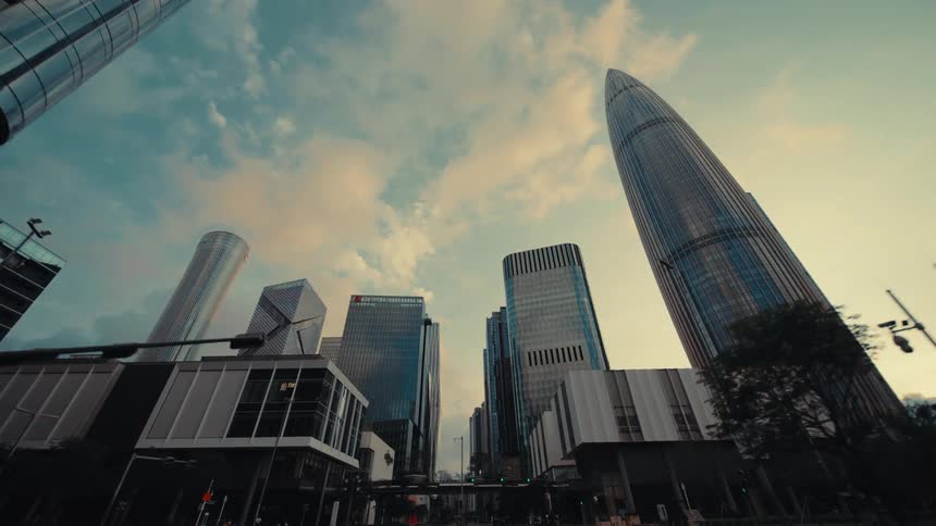 A low-angle dolly shot slowly moves through a modern city financial district, looking up at impressive glass skyscrapers against the sky