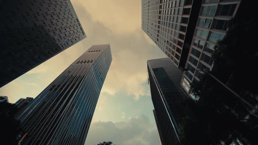 A slow pull-back shot reveals the towering glass skyscrapers of a modern city against a warm, cloudy sky