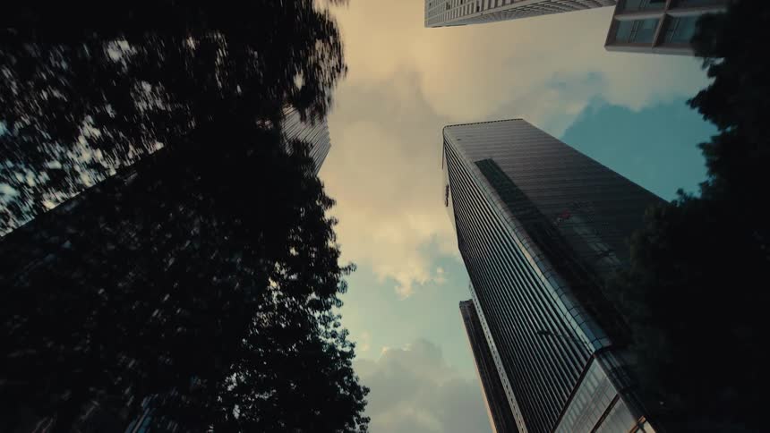 A slow pull-back shot reveals the towering glass skyscrapers of a modern city against a warm, cloudy sky
