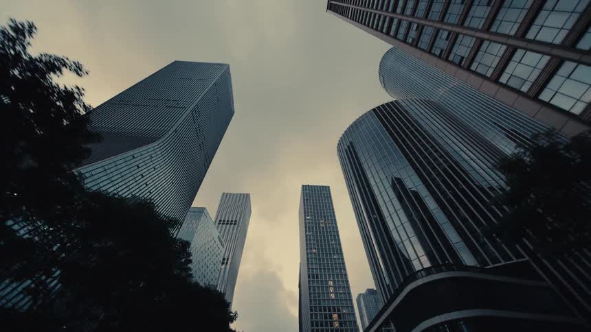 A slow dolly-out, low-angle shot reveals towering modern glass skyscrapers against a moody, overcast sky