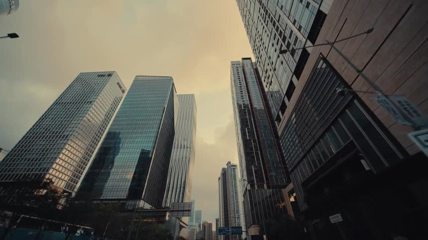 A slow, cinematic push-in shot from a low angle captures the imposing glass skyscrapers of a modern metropolis against a dusky sky