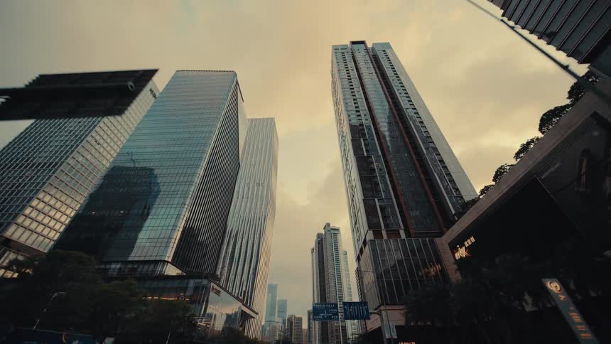 A slow, cinematic push-in shot from a low angle captures the imposing glass skyscrapers of a modern metropolis against a dusky sky