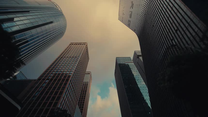 A low-angle dolly shot looking up at impressive modern glass skyscrapers while driving through a city canyon