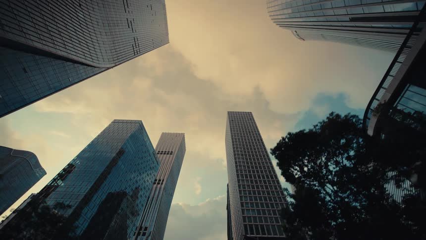 A slow, low-angle tracking shot through a modern city's financial district reveals towering glass skyscrapers against a dramatic sky