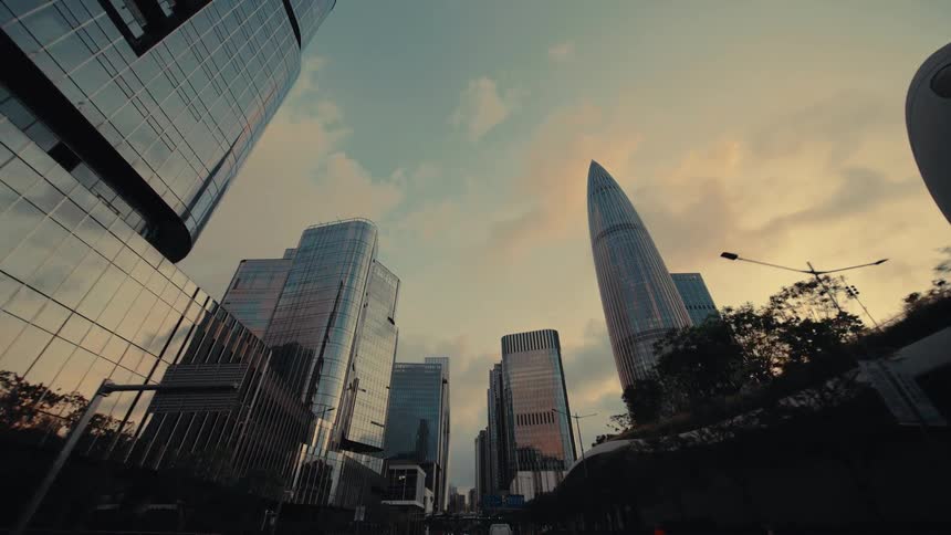 A slow, low-angle forward tracking shot reveals the impressive skyline of a modern, futuristic city with glass skyscrapers at sunset