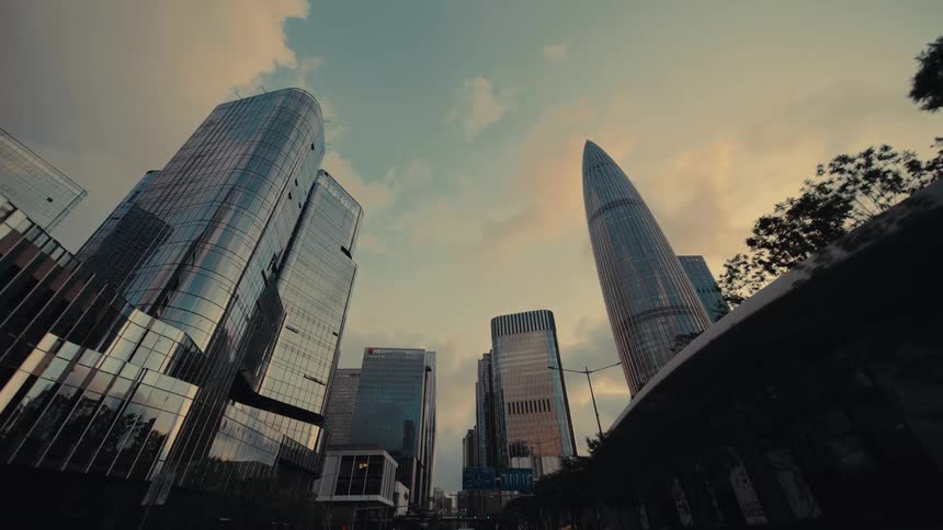 A slow, low-angle forward tracking shot reveals the impressive skyline of a modern, futuristic city with glass skyscrapers at sunset