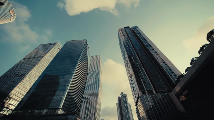 A stylized low-angle view slowly pulls back from a group of towering glass skyscrapers in a modern city's financial district