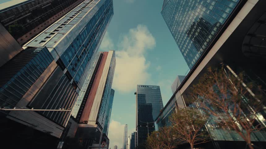 A slow-motion, low-angle forward tracking shot through a modern city filled with impressive glass skyscrapers