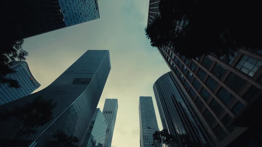 A cinematic low-angle dolly shot moves backward through a modern city, revealing towering glass skyscrapers against an overcast sky
