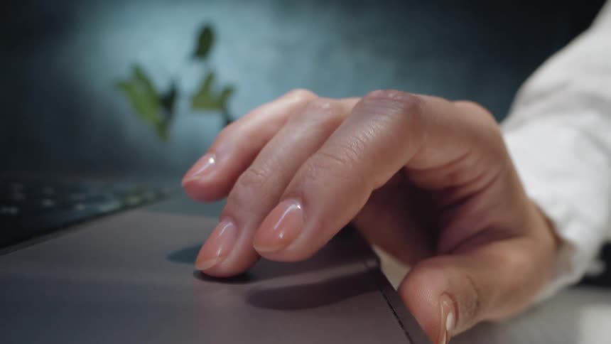 Extreme close-up of a person's hand using the trackpad on a laptop computer