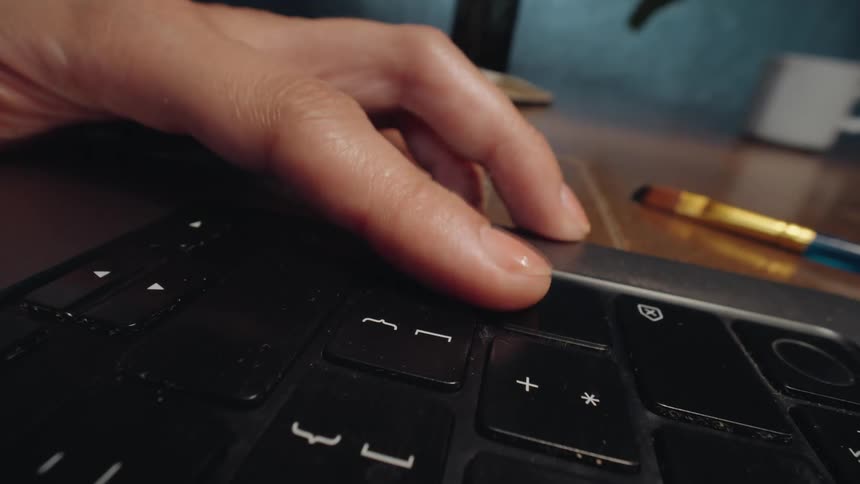 A dynamic camera push-in focuses on a hand pressing the power button to turn on a laptop computer