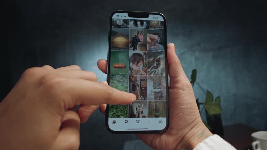A close-up of a person's hands holding a smartphone and scrolling through a social media feed filled with various photos and videos