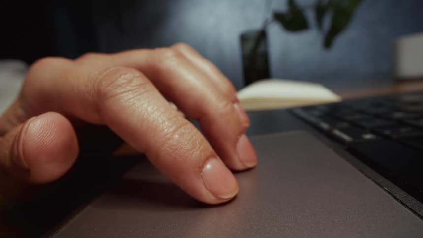 A close-up macro shot of a person's hand tapping and scrolling on a laptop's trackpad