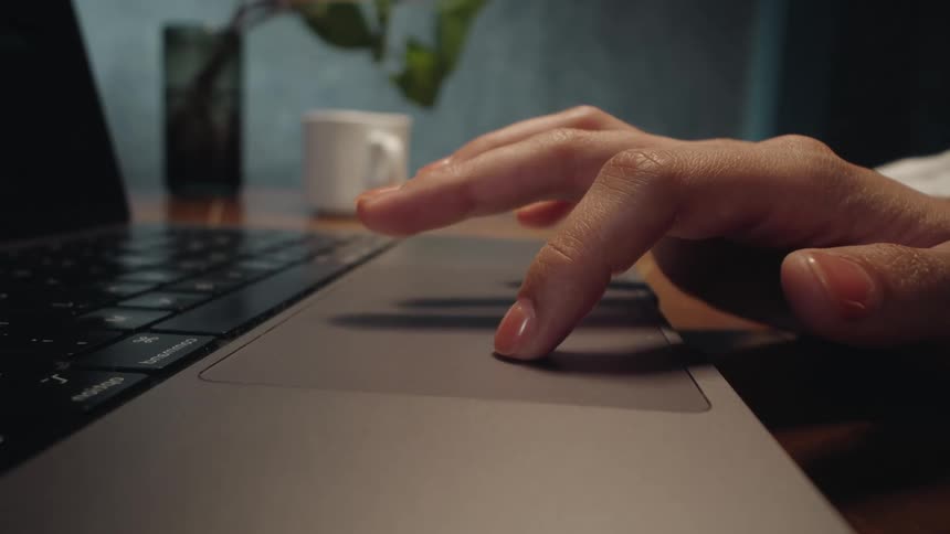 Close-up side view of a woman's hand with manicured nails tapping on a laptop trackpad