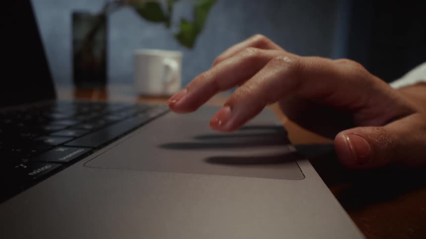 A close-up shot of a woman's hand slowly scrolling and tapping on a laptop trackpad in a dimly lit room