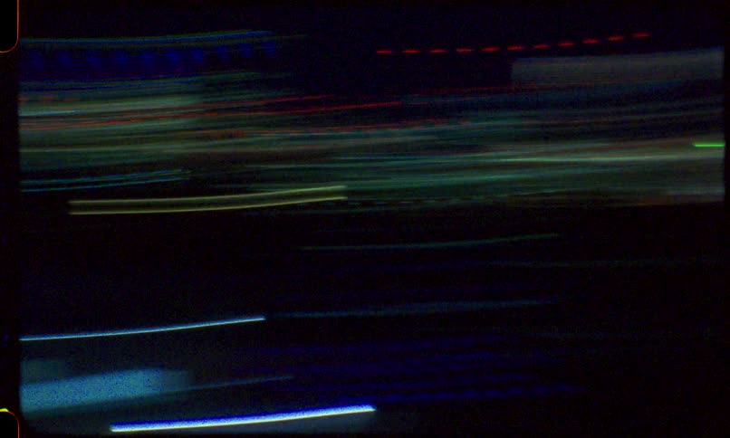 A disorienting and abstract view of colorful city lights at night, seen from a moving train, creating streaky light trails