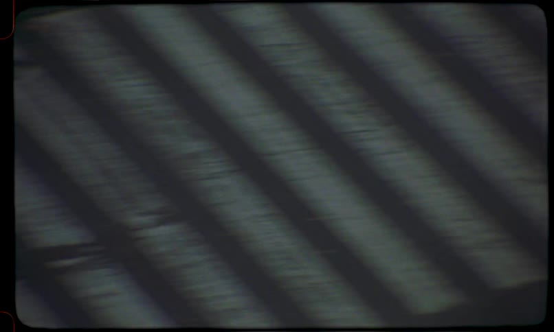 A shaky, high-angle, vintage 8mm film shot looking down at a city street crosswalk