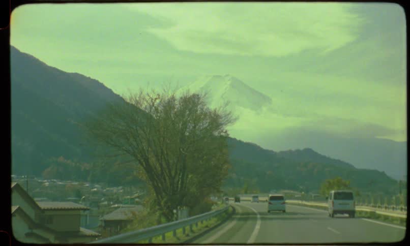 POV shot from a car driving along a highway in Japan with a clear view of the iconic Mount Fuji, captured on vintage film