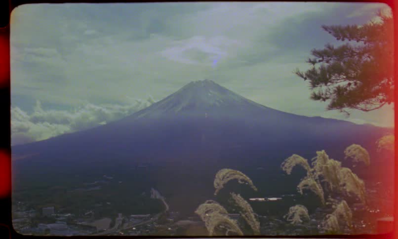 Vintage 8mm film captures a hazy, scenic view of Japan's Mount Fuji with pampas grass swaying in the breeze