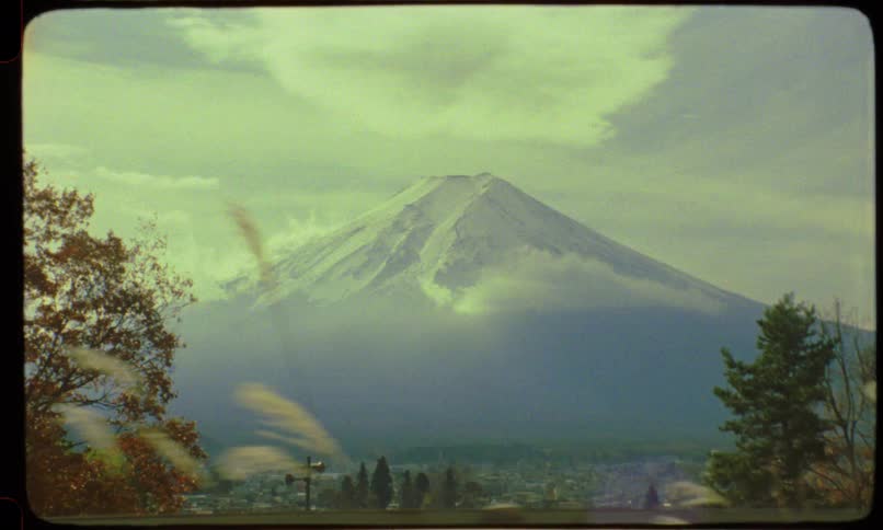 Vintage film captures a scenic drive past the majestic snow-capped Mount Fuji in Japan during autumn, with colorful foliage in the foreground